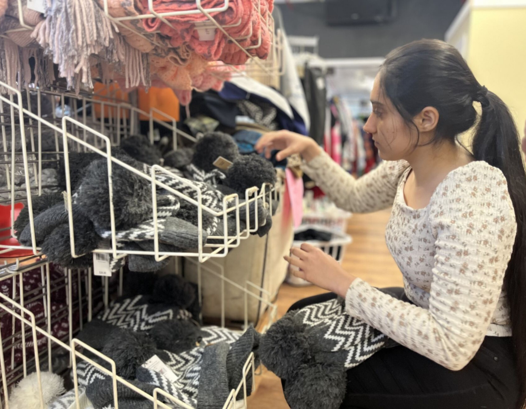 A person knelt down in front of shelves of clothing