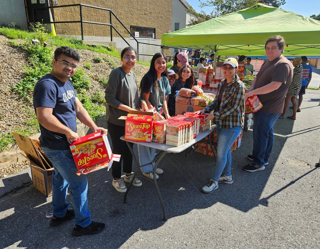 A group of people outside surrounding a table with boxes and one person carrying a box