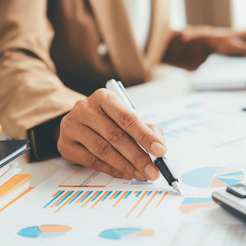 A person's hand holding a pen, hovering over papers with multiple charts.