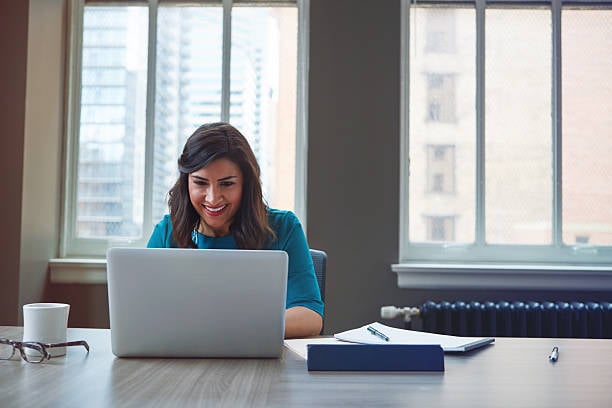 A woman grinning while looking at her laptop. A woman grinning while looking at her laptop.